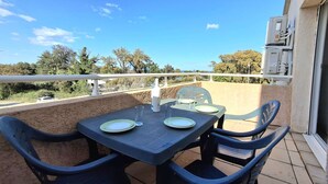 Ein Balkon mit Tisch und Stühlen, Geländer und Blick auf Bäume und eine Straße.