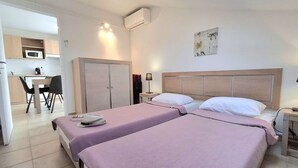 Ein Hotelzimmer mit zwei Betten, einem Schreibtisch, einem Stuhl, einem Kleiderschrank und einer Küchenzeile.