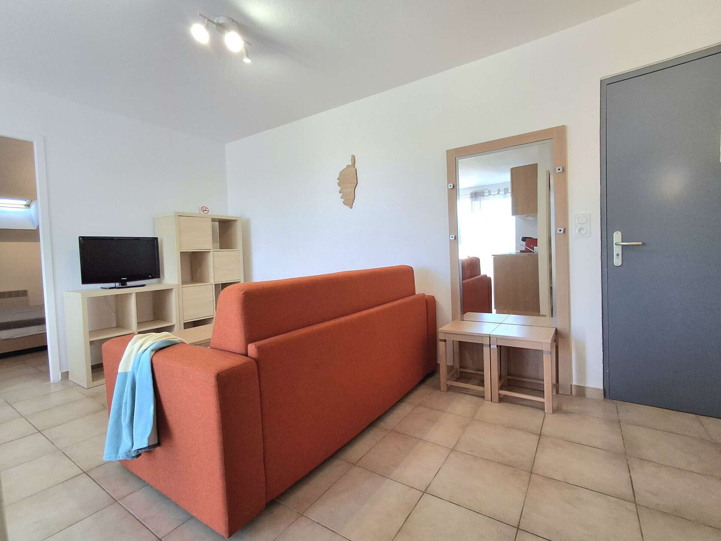 Un salon avec un canapé, un téléviseur posé sur un meuble, un buffet en bois et une porte.
