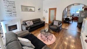 A modern living room with a fireplace, a dining area, and a kitchen visible through an archway. - Holiday house Lona (Crikvenica)