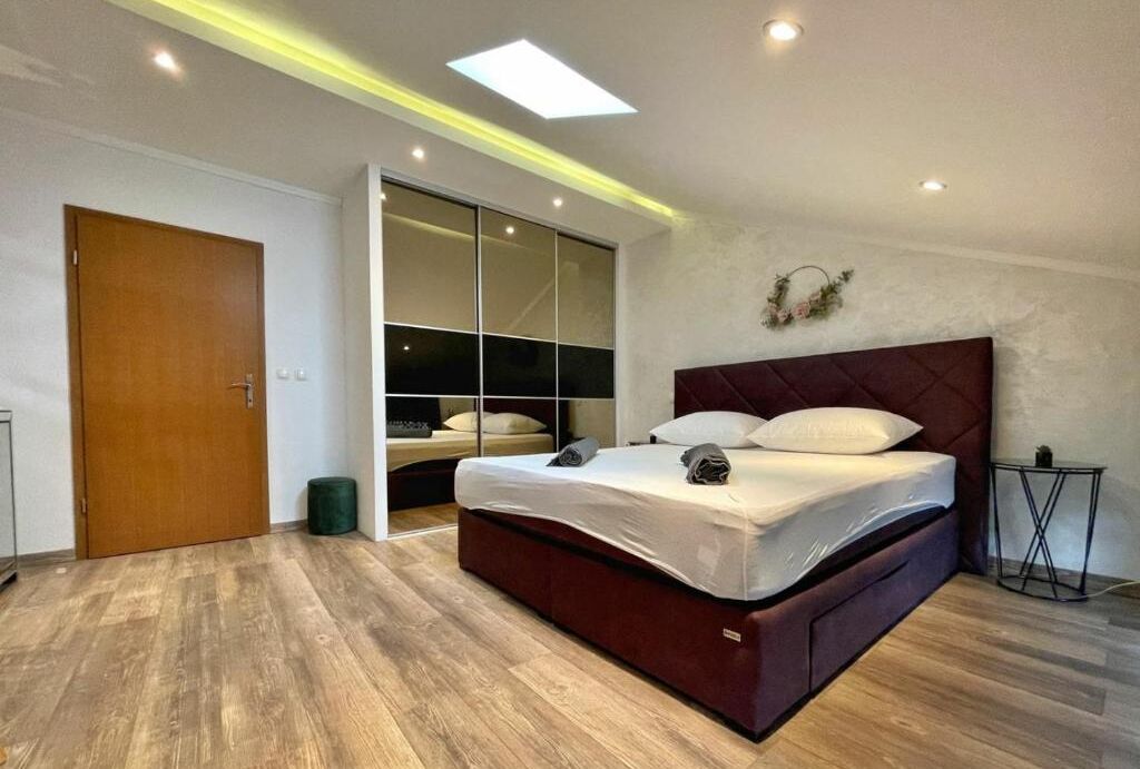 A modern bedroom with a large bed, a sliding door closet, and recessed ceiling lighting.