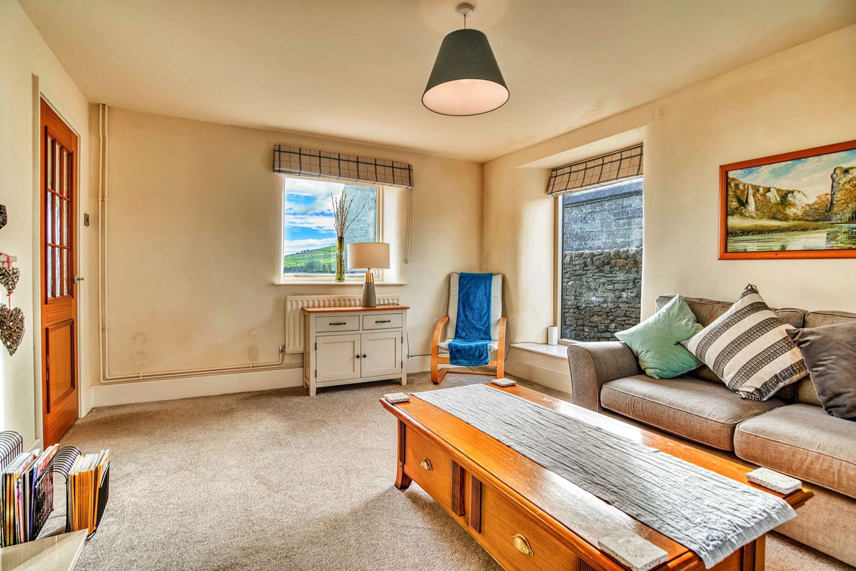 A room with a wooden desk, a sofa, a bench, a radiator, a window with a view, and a painting on the wall.