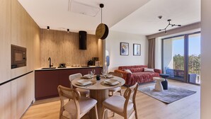 Una cucina moderna con elementi in legno, un'area pranzo con tavolo rotondo e un soggiorno con divano rosso e balcone.