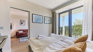 Una camera da letto moderna con un letto grande, un divano rosso sullo sfondo e un balcone con vista.