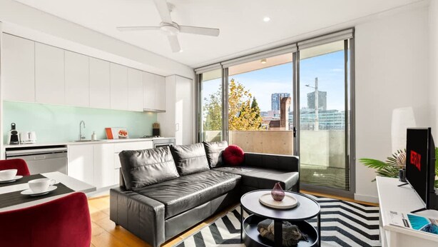 Um apartamento moderno com cozinha, sala de estar com sofá e mesa de centro, e varanda com vista para a cidade.