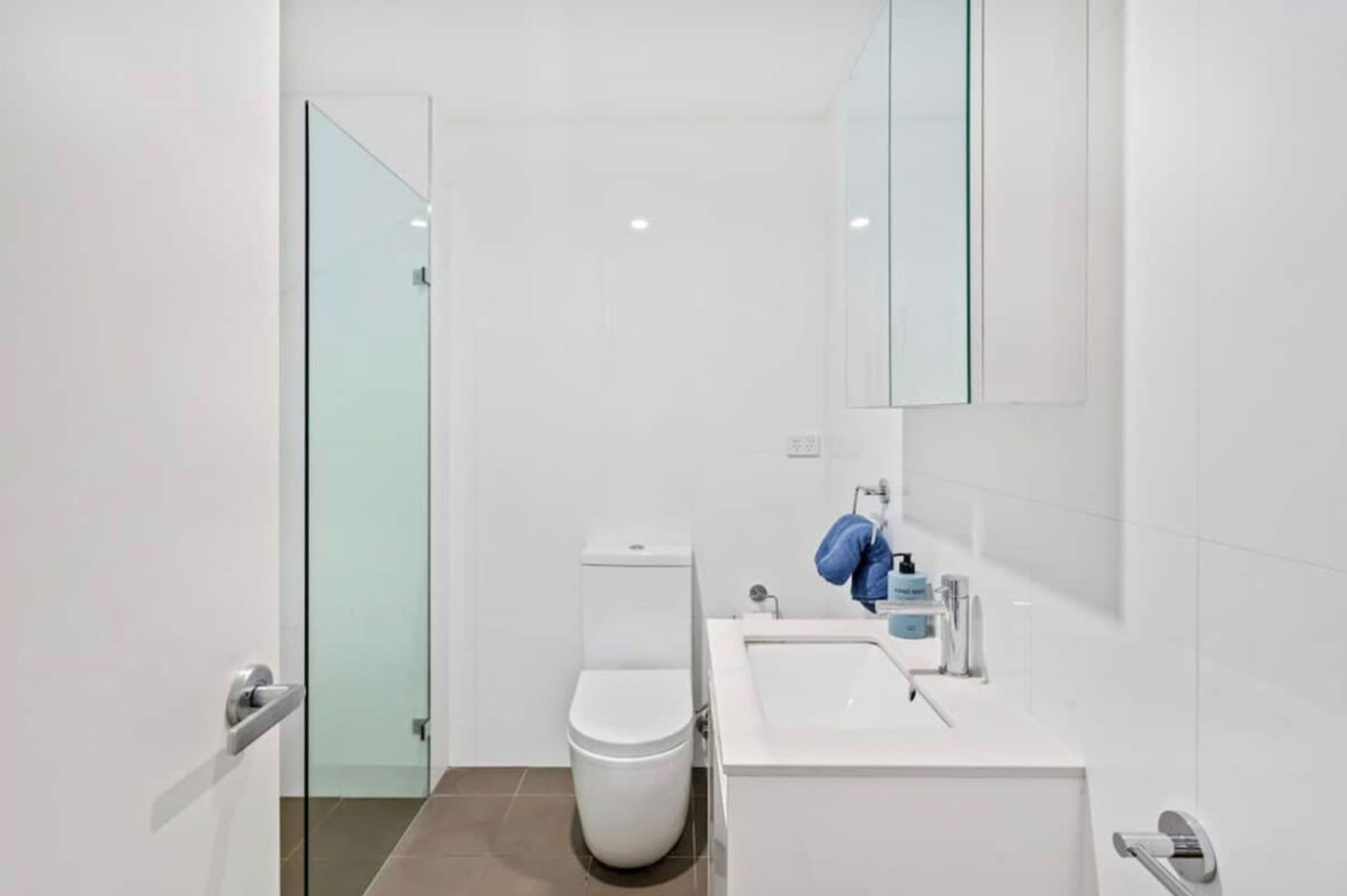 Une salle de bain moderne avec une douche à parois de verre, des toilettes blanches et un lavabo avec un miroir au-dessus.