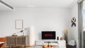 Una sala moderna con un televisor de pantalla plana mostrando 'NETFLIX', un mueble de madera, una consola blanca y un ventanal con vistas.