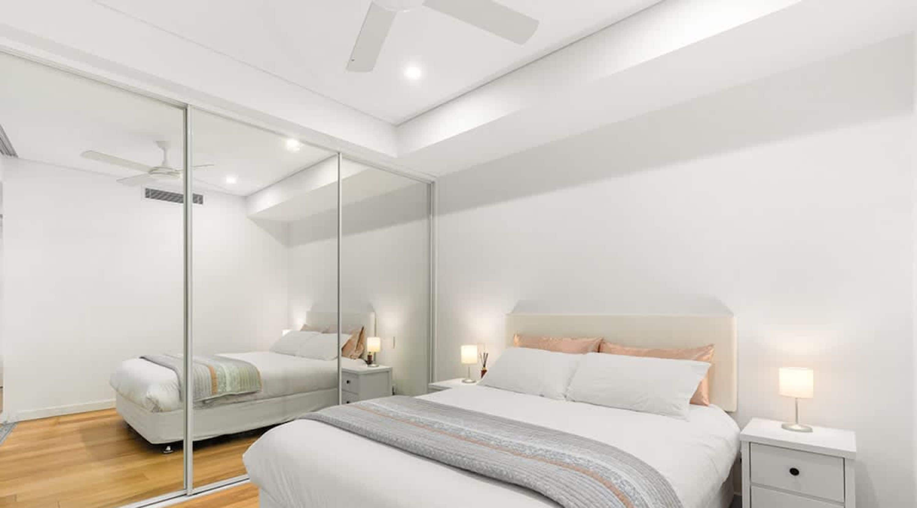 A modern bedroom with a large bed, bedside tables, a mirror, and a ceiling fan.