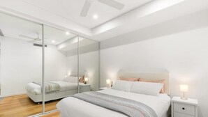 Un dormitorio moderno con una cama grande, mesitas de noche, un espejo y un ventilador de techo.
