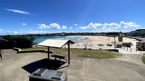 A beachside area with a covered seating area, a concrete walkway, and a view of the beach and ocean. - Cozy Beachfront Studio With Aircon (Sydney)