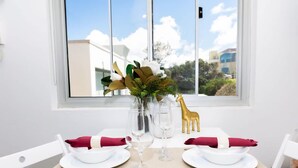 A dining table set with white plates, red napkins, and clear glassware, positioned by a window with a view of buildings and trees. - Cozy Beachfront Studio With Aircon (Sydney)