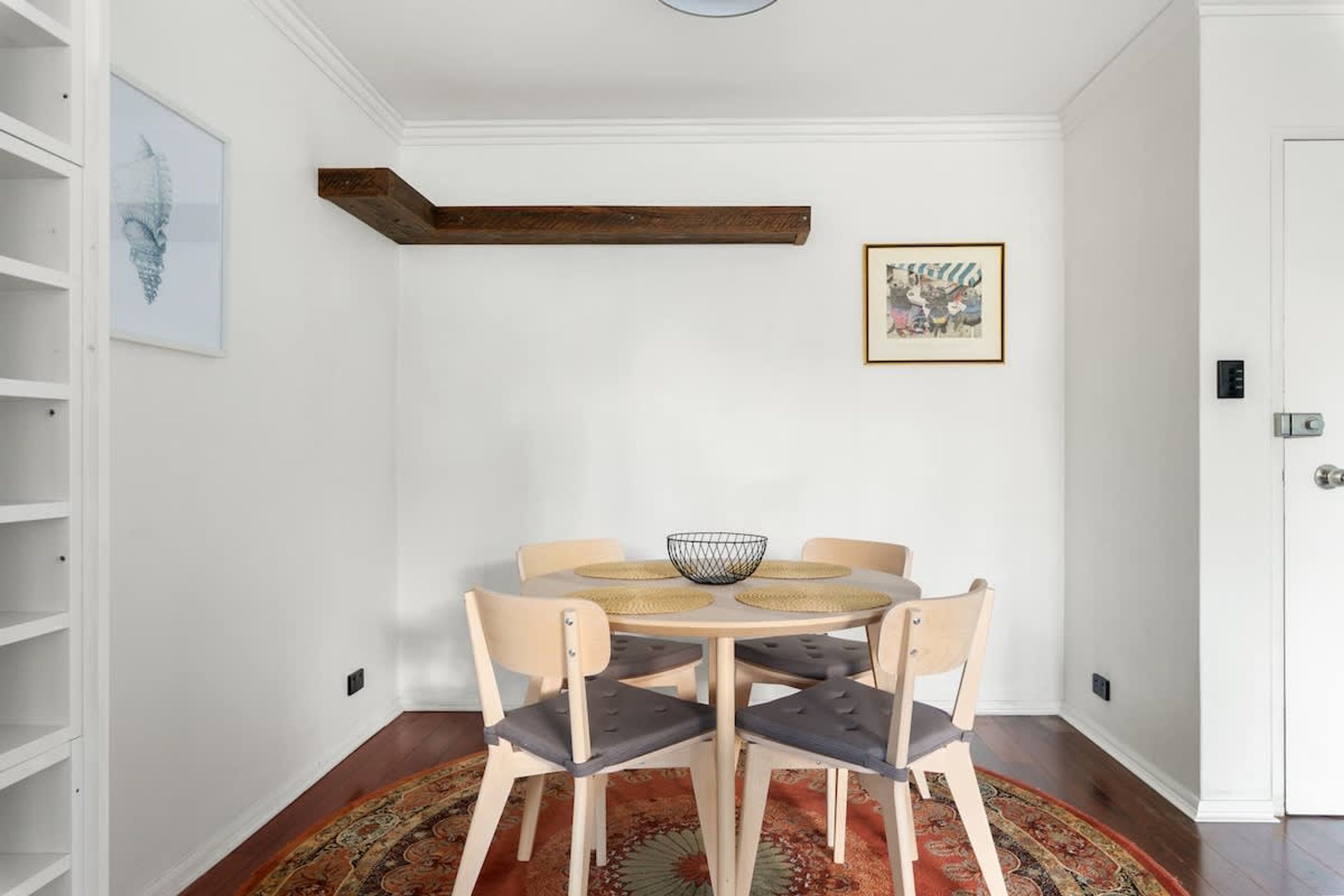 Un comedor con una mesa redonda, cuatro sillas, una cesta tejida y una alfombra estampada.