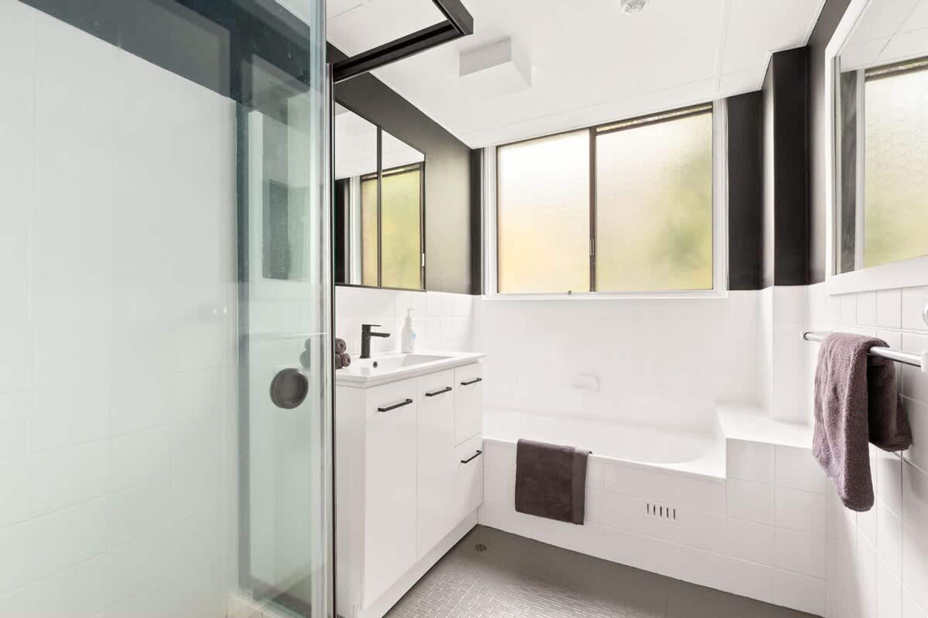 Un bany modern amb plat de dutxa de vidre, un lavabo blanc i una banyera.