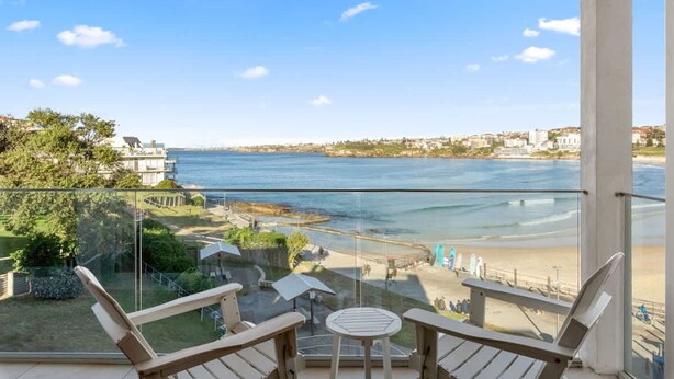 A balcony with a view of the sea and beach, featuring outdoor seating and a glass railing. - Beachfront Luxury 3 Beds With Ocean View Balcony (Sydney)