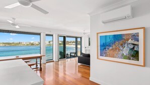 A spacious living area with a large window overlooking a coastal view, a ceiling fan, and a framed painting on the wall. - Beachfront Luxury 3 Beds With Ocean View Balcony (Sydney)