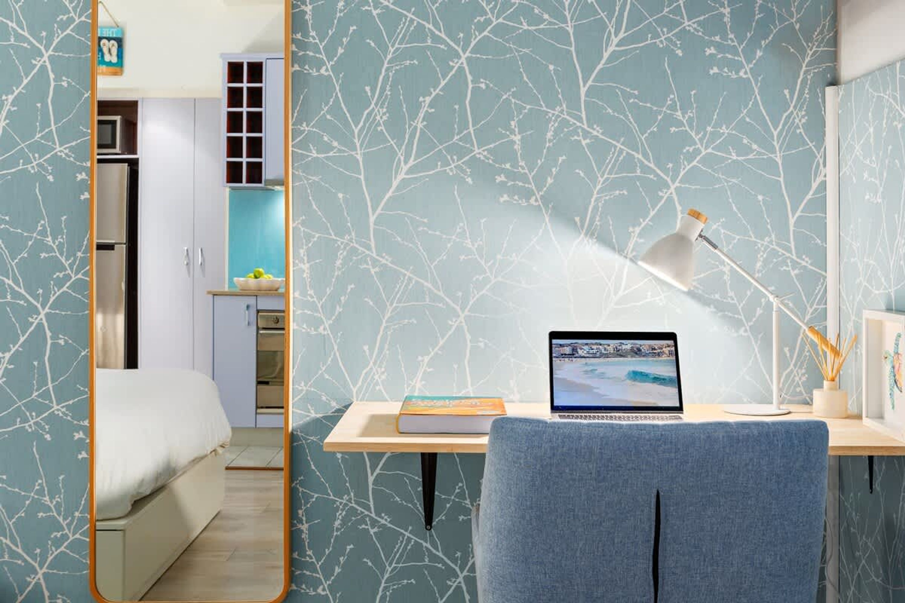 Une chambre à coucher avec un lit, un bureau avec un ordinateur portable, une chaise, un miroir et une armoire.