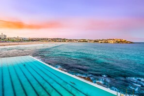 Escena costera con piscina, playa y edificios al fondo.