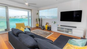 Una sala de estar moderna con un sofá grande, un televisor de pantalla plana y vistas al océano.