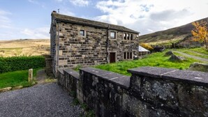 Edificio de piedra con un pequeño porche y una puerta, rodeado de césped y un muro de piedra.