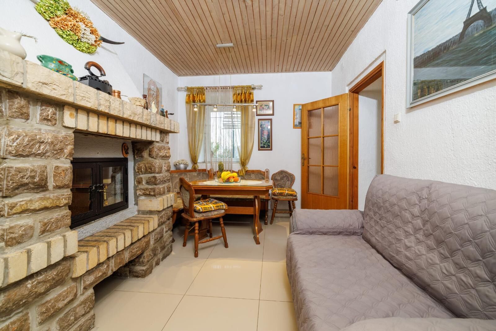 A cozy living room with a stone fireplace, a dining area with a table and chairs, and a grey sofa.