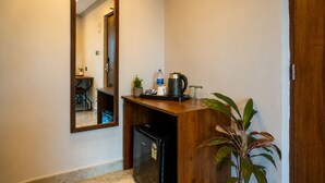 Zona de recepción de un hotel con un escritorio de madera, un refrigerador, una cafetera, una botella de agua y una planta en maceta.