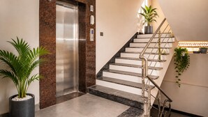 Un ascensor moderno con detalles metálicos, una escalera con barandilla de metal y plantas en macetas.