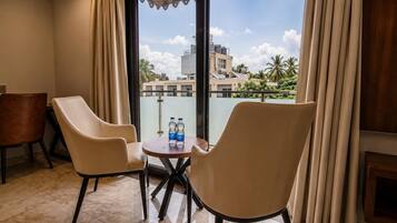 Quarto de hotel com varanda, duas cadeiras, uma mesinha e duas garrafas de água.