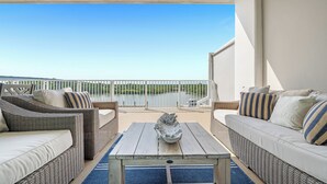 A balcony with wicker furniture, a table, and a view of a body of water.