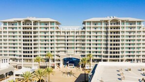 A large hotel with multiple floors, a central entrance, and a parking area with palm trees.