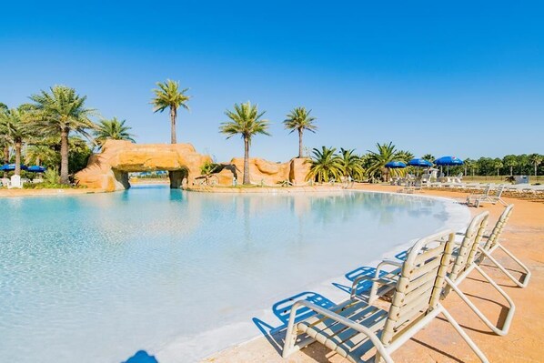 A pool area with lounge chairs and umbrellas, palm trees, and a rock formation.