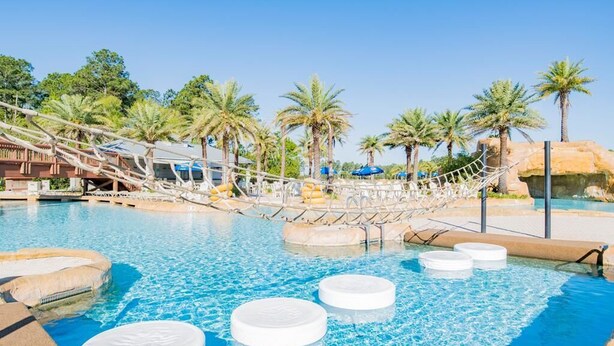 A pool area with palm trees, a wooden bridge, and lounge chairs.