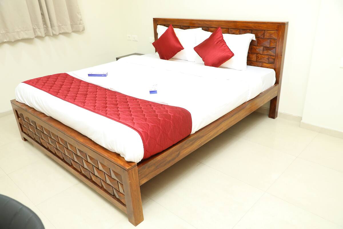 A neatly made bed with a wooden frame, red and white bedding, and two red pillows.