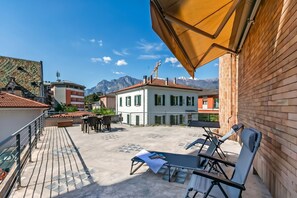A rooftop terrace with outdoor seating, a view of mountains, and a building with a red roof. - The Arco Round House With Terrace & Parking (Arco)