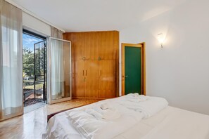 A bedroom with a bed, a wooden wardrobe, a green door, and a sliding glass door leading to an outdoor area.