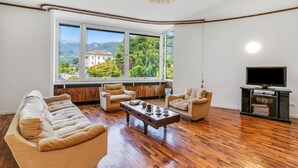 Un salón amplio con un gran ventanal, suelo de madera y televisor.