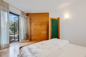 A bedroom with a bed, a wooden wardrobe, a green door, and a sliding glass door leading to an outdoor area. - The Arco Round House With Terrace & Parking (Arco)