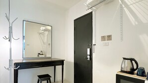 A compact room with a desk, a small stool, a black door, a mini fridge, and a wall-mounted shelf. - Chatel Samyan BKK (Bangkok)