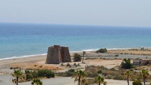 A coastal view with a historical stone tower, sandy beach, and sparse vegetation. - Macenas 85.2 Apartments (family and pets) (AN)