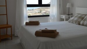 A neatly made bed with two rolled towels, a bedside table with a lamp, and a window with a view of buildings and hills. - Macenas 85.2 Apartments (family and pets) (AN)