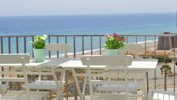 A balcony with white chairs and tables, overlooking a beach and the ocean. - Macenas 85.2 Apartments (family and pets) (AN)