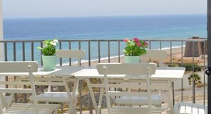 A balcony with white chairs and tables, overlooking a beach and the ocean. - Macenas 85.2 Apartments (family and pets) (AN)