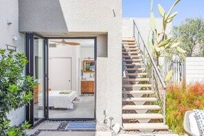 A modern home with a glass door leading to a bedroom, a staircase, and a garden with cacti and shrubs. - Casa Soleil - A Family Friendly Oasis (Palm Springs)