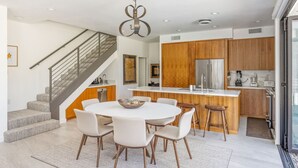 Una cocina moderna con una isla central, armarios de madera y electrodomésticos de acero inoxidable, y una escalera que conduce a un nivel superior.