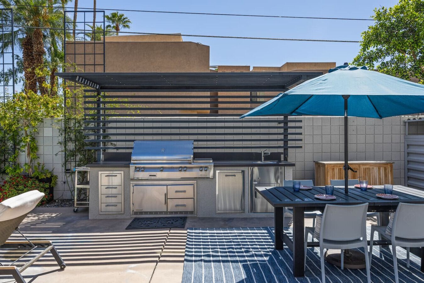 An outdoor kitchen area with a grill, dining table, chairs, and a large umbrella.