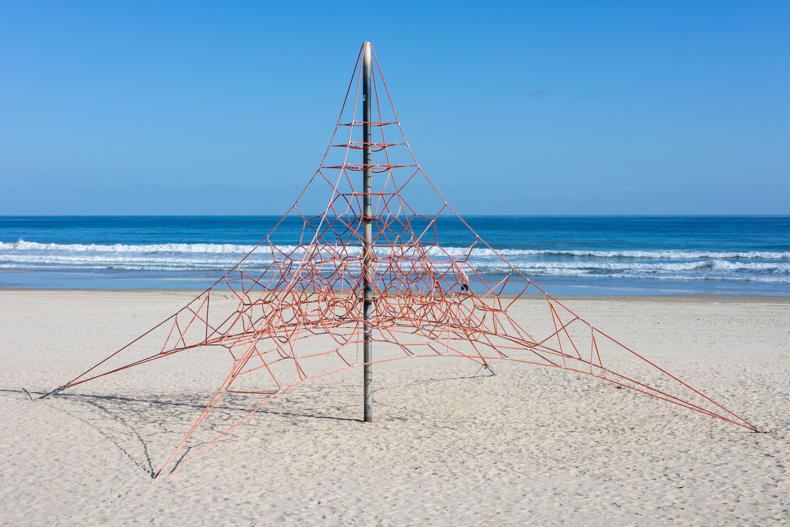 Una escultura metàl·lica geomètrica sobre una platja sorrenca amb l'oceà de fons.