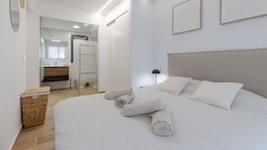 Een moderne slaapkamer met een groot bed, een nachtkastje, een lamp en uitzicht op de badkamer.