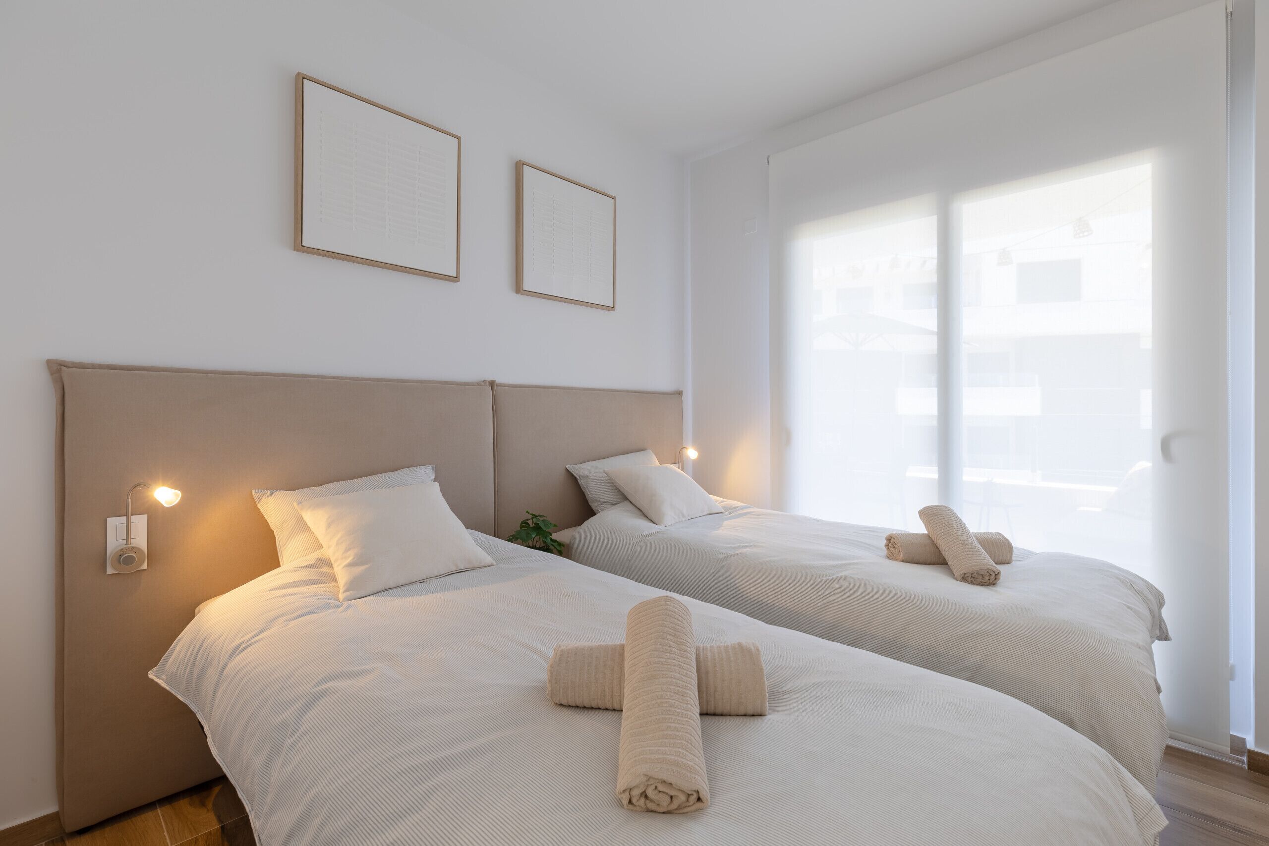 Hotelkamer met twee bedden, elk voorzien van een hoofdeinde, nachtkastje en een wandlamp.