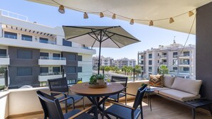 Een balkon met een ronde tafel, stoelen, een bank en een parasol.