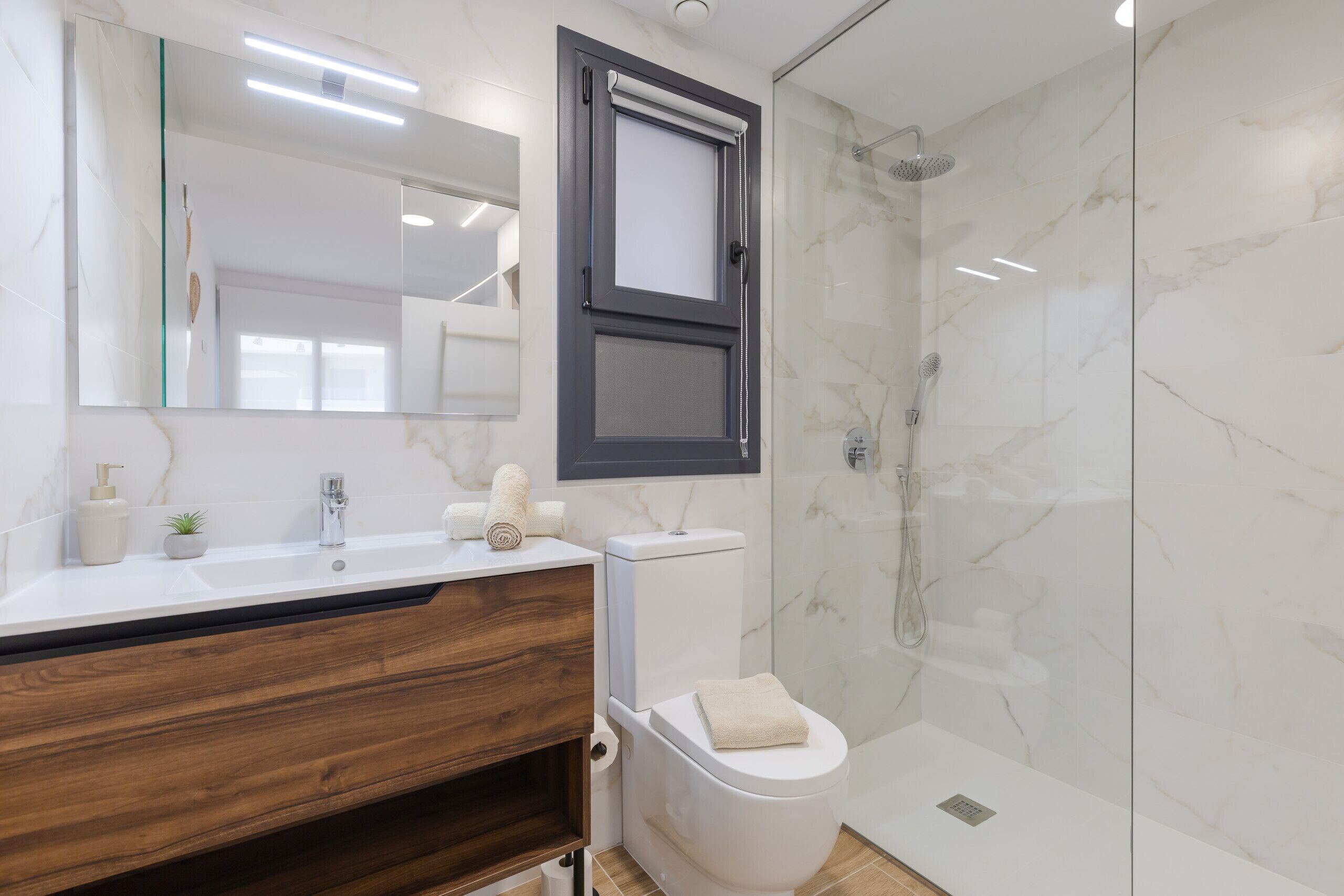A modern bathroom with a marble shower, a wooden vanity, and a toilet.