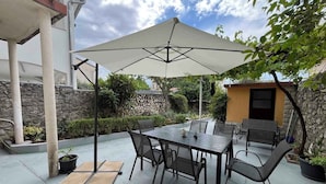 Une terrasse extérieure avec une table et des chaises sous un grand parasol, entourée de murs en pierre et de verdure.